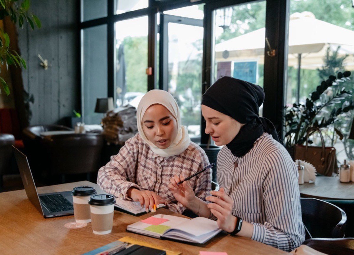 Dua peserta berhijab belajar bersama, satu sedang menjelaskan catatan